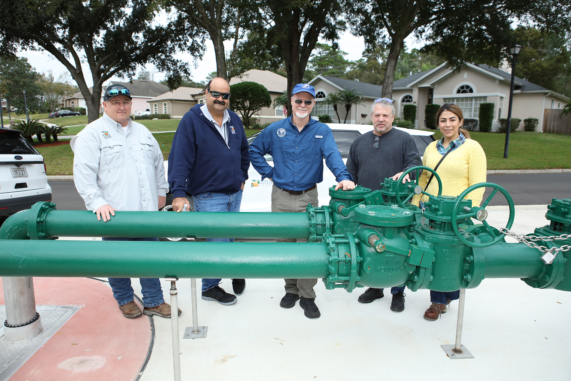 Four men and one woman posing for picture with double green pipe/valve system on sidewalk in neighborhood.